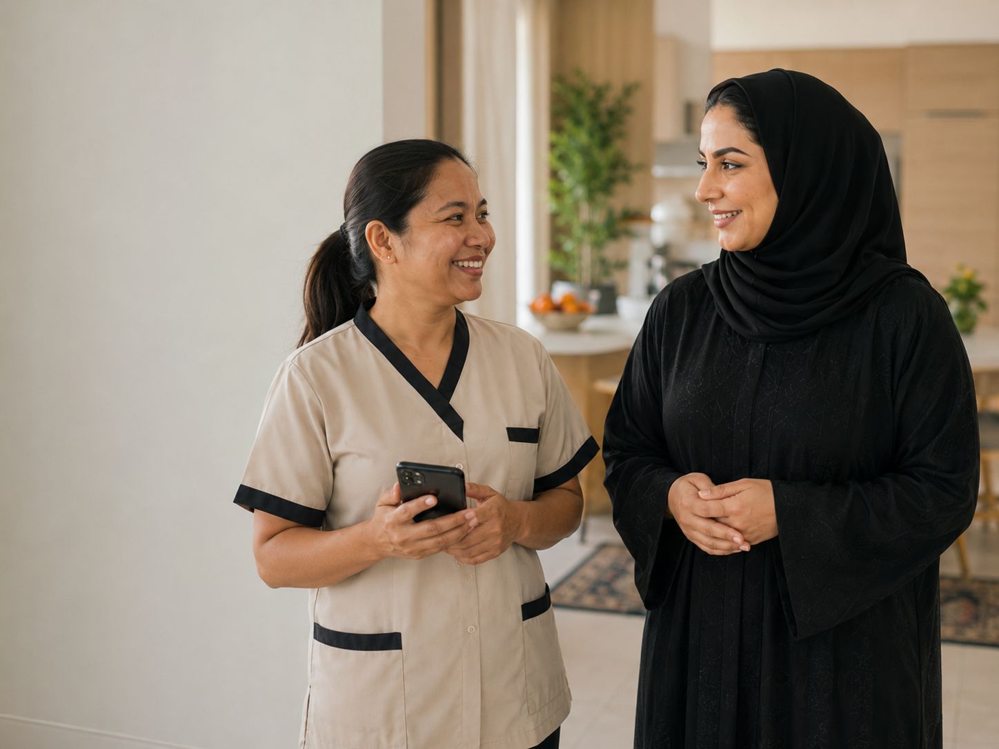 A Kuwaiti household member talking with her domestic worker, who holds her phone with the Khidma app